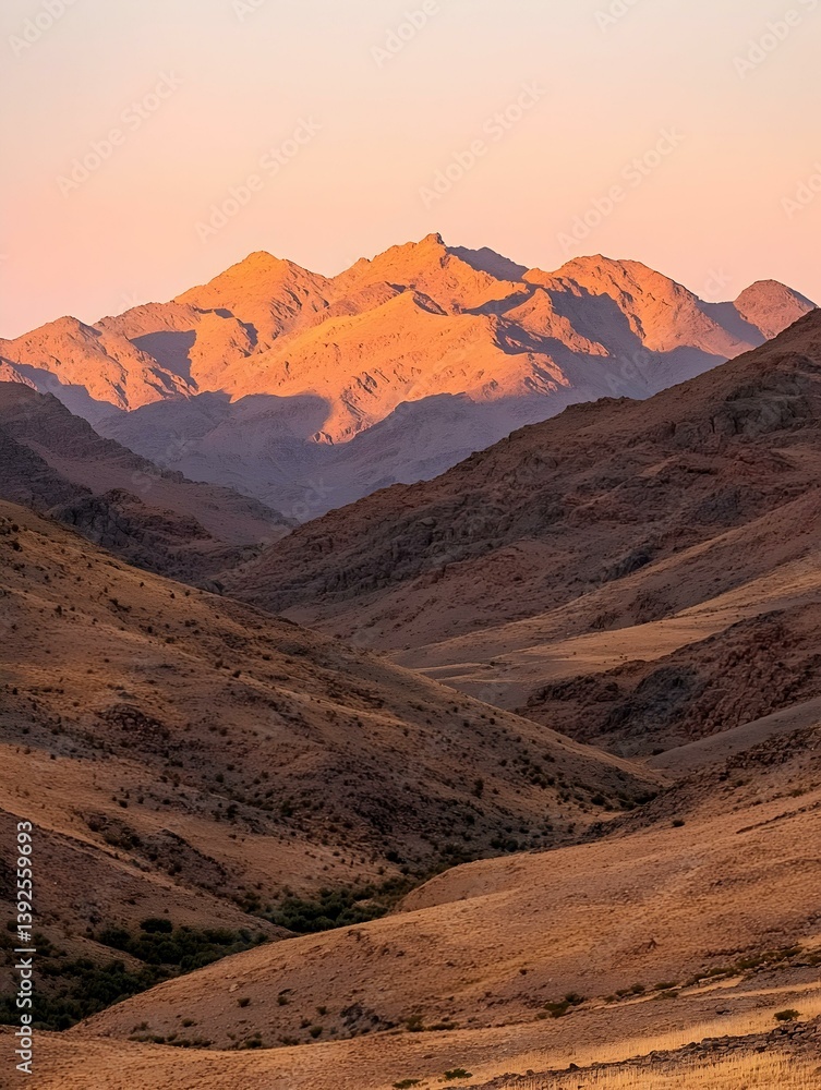 Naklejka premium Majestic sunset illuminating a breathtaking mountain range. Golden hour casts warm hues across rugged peaks and valleys.