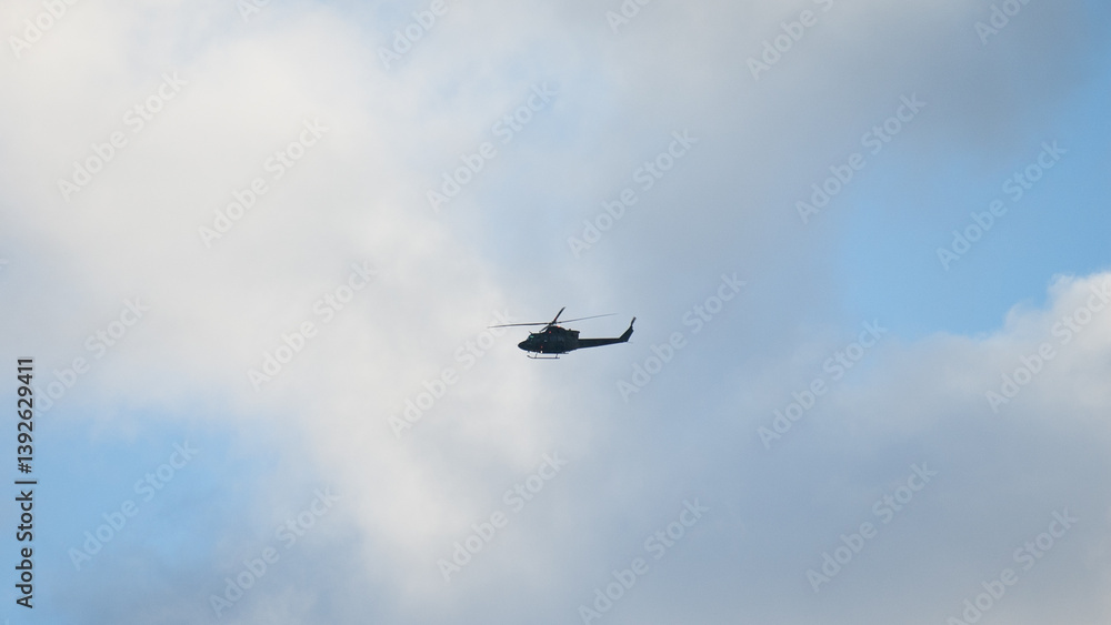 Military helicopter in the sky during flight against blue sky and gray clouds Military helicopter in the sky during flight against blue sky and gray clouds