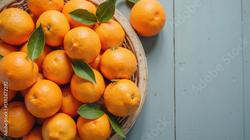 Fresh oranges in woven basket with green leaves on light blue wooden surface create vibrant and inviting scene