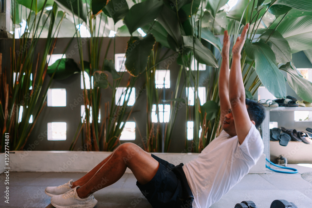 Fototapeta premium Man doing crunches at his home gym with tropical plant background