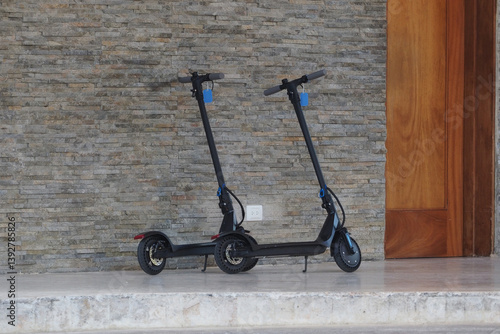 Two electric scooters parked inside a contemporary building near a stone wall. 
