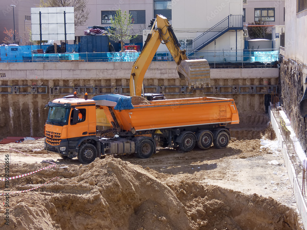 Construction site with orange dump truck and excavator digging at urban location during daylight hours