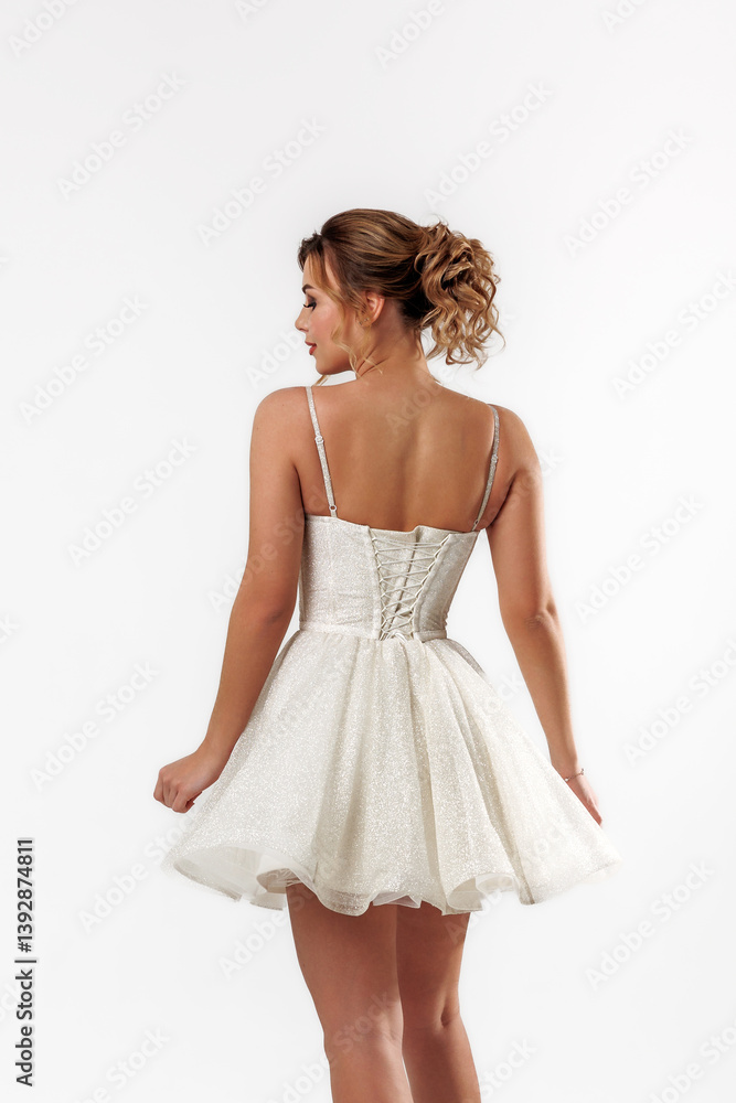 Elegant young woman in a shimmering silver dress poses gracefully from the back against a simple white background Elegant young woman in a shimmering silver dress poses gracefully from the back against a simple white background
