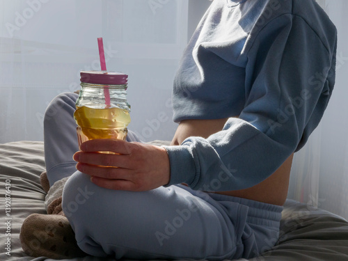 Pregnant woman sits comfortably on bed, sipping fruit juice from glass jar, enjoying peaceful moment. Pregnant lifestyle captured in soft light. Pregnant relaxation scene in cozy setting. 