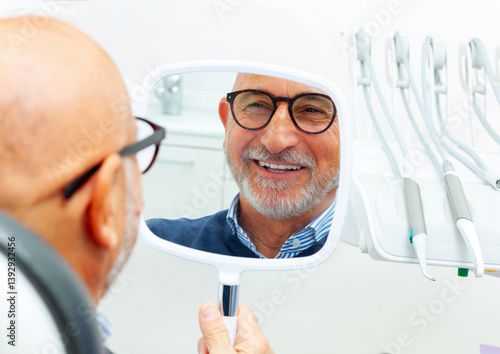 Senior man checking new teeth in the mirror at the dental clinic