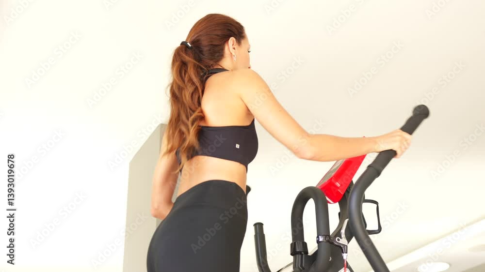 Athletic woman works out on elliptical machine in a sleek gym, focusing on cardio fitness, movement, and a consistent active lifestyle. Athletic woman works out on elliptical machine in a sleek gym, focusing on cardio fitness, movement, and a consistent active lifestyle.
