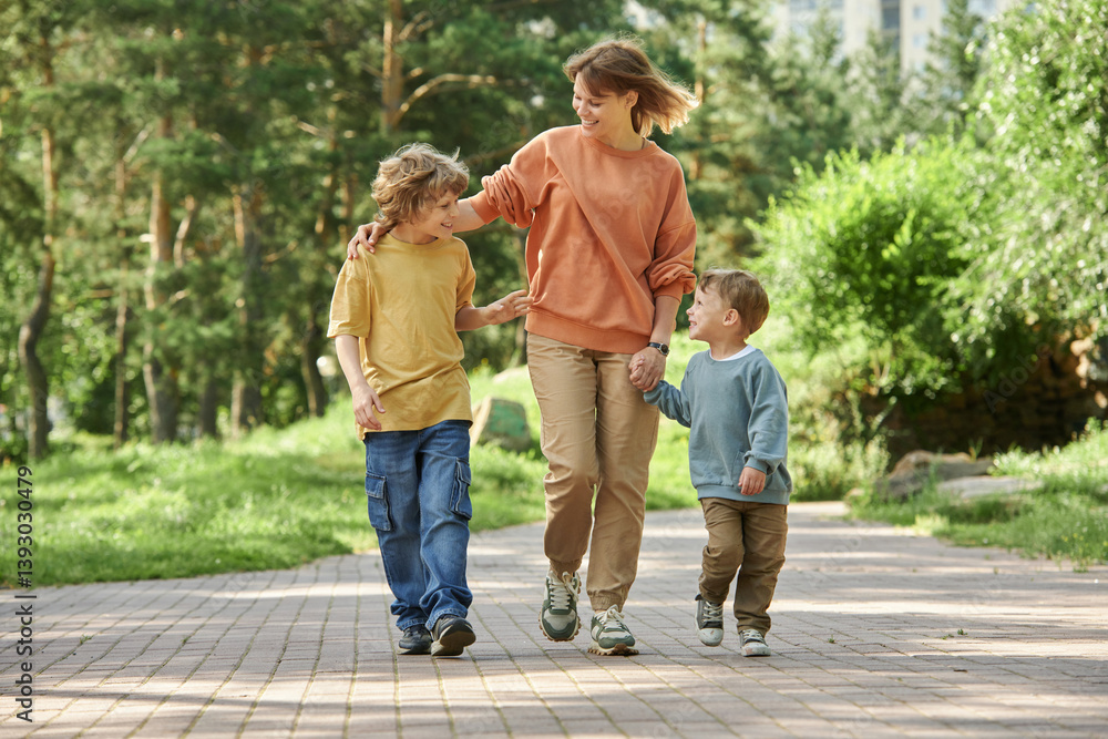 Full length front view of cheerful mother with two boys holding hands while walking towards camera in green park copy space Full length front view of cheerful mother with two boys holding hands while walking towards camera in green park copy space