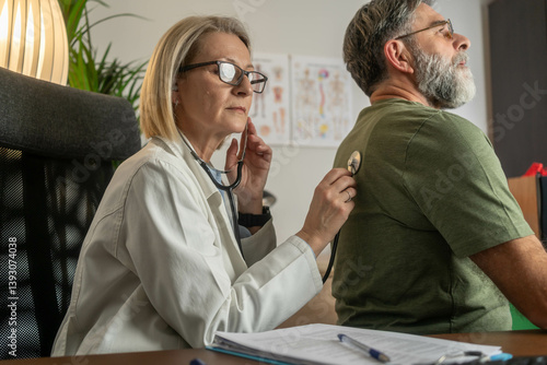 Female doctor using stethoscope to listen to male patient's lungs during medical examination in modern clinic, showing care, professionalism, and health checkup.