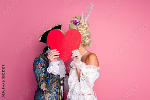 Foto Elegant couple in historical costumes holding a heart on a pink background, perfect for romantic or vintage-themed designs