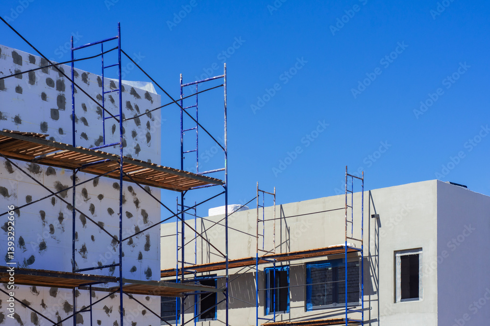 A building under construction is surrounded by scaffolding against a blue sky. Progress of modern architecture. A building under construction is surrounded by scaffolding against a blue sky. Progress of modern architecture.