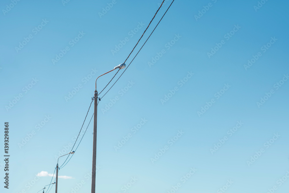 Street lamp stands tall with power lines stretching across a clear blue sky. Urban infrastructure in a minimalist style. Street lamp stands tall with power lines stretching across a clear blue sky. Urban infrastructure in a minimalist style.
