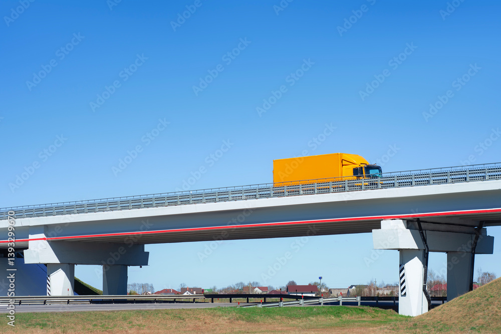 Fototapeta premium Mockup yellow truck travels on a highway overpass under a clear blue sky. Concept transportation and logistics.