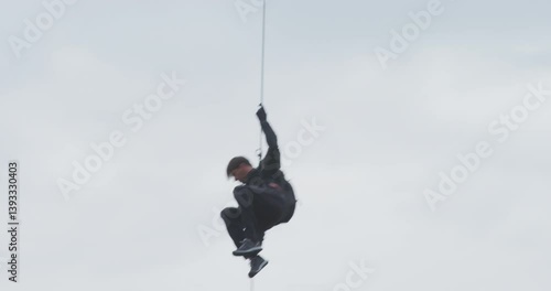 Man rappelling from helicopter with overcast sky - low shot