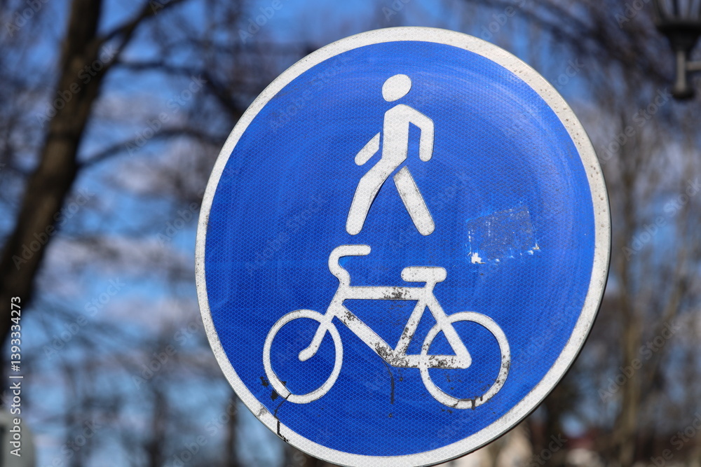 A person rides a bike beside a blue and white sign, outdoors.