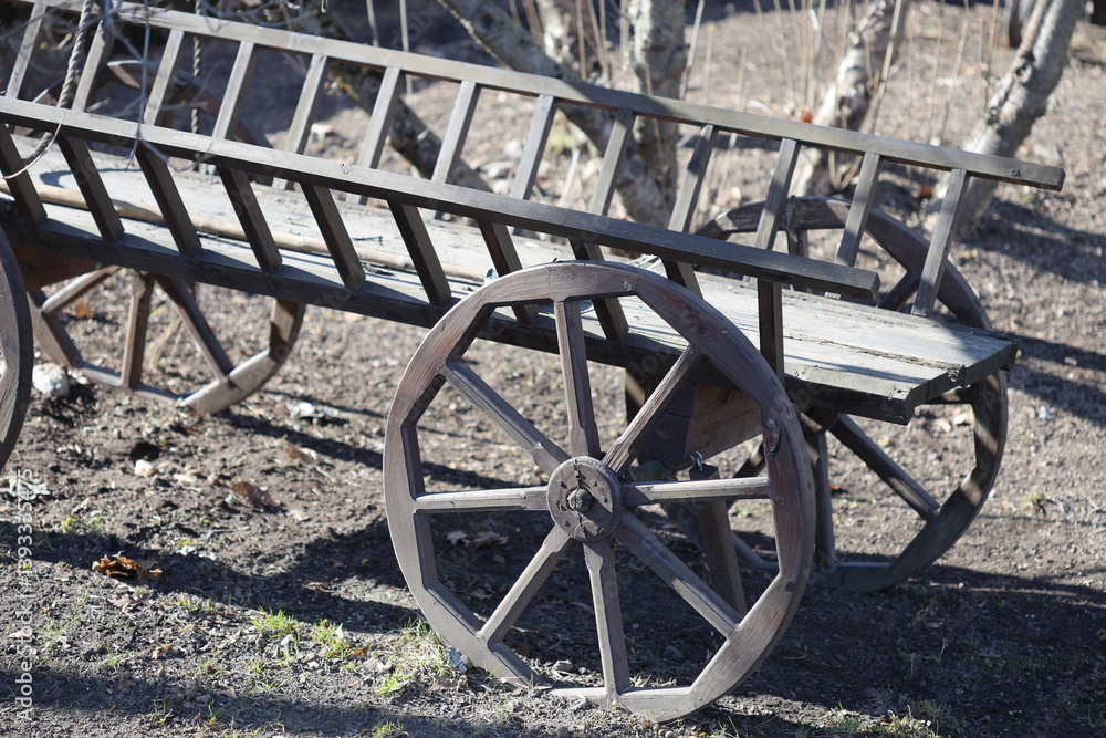 A simple wooden bench sits beside a traditional wooden wagon, perfect for rustic outdoor scenes or vintage-themed settings.