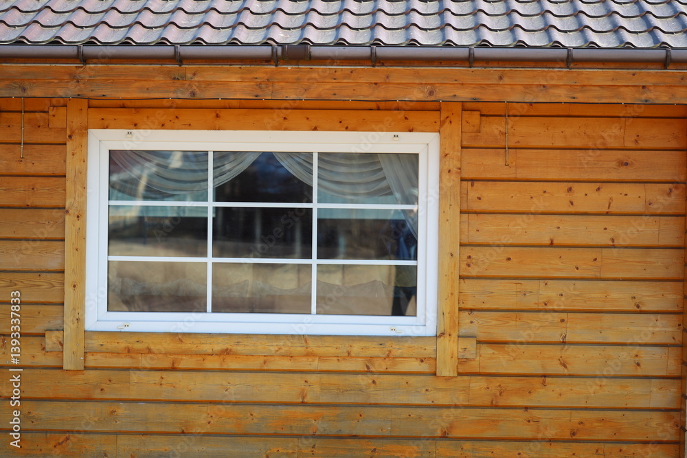 A domestic cat is sitting in the window of a traditional wooden house.