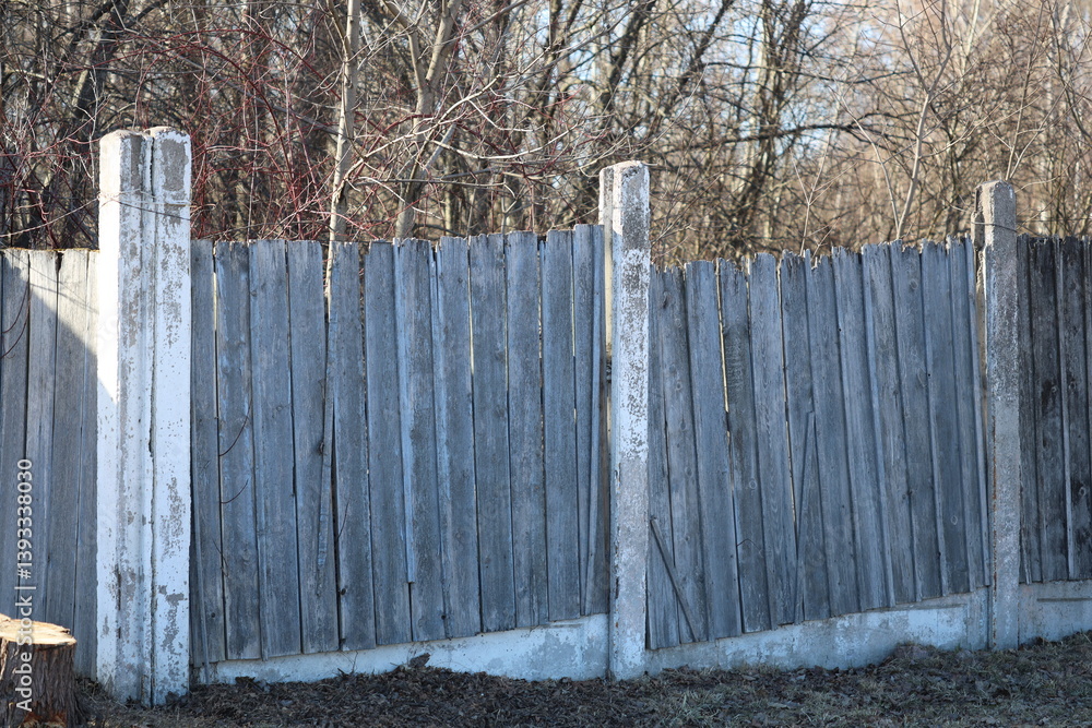 A fire hydrant sits next to a wooden fence in a outdoor setting.