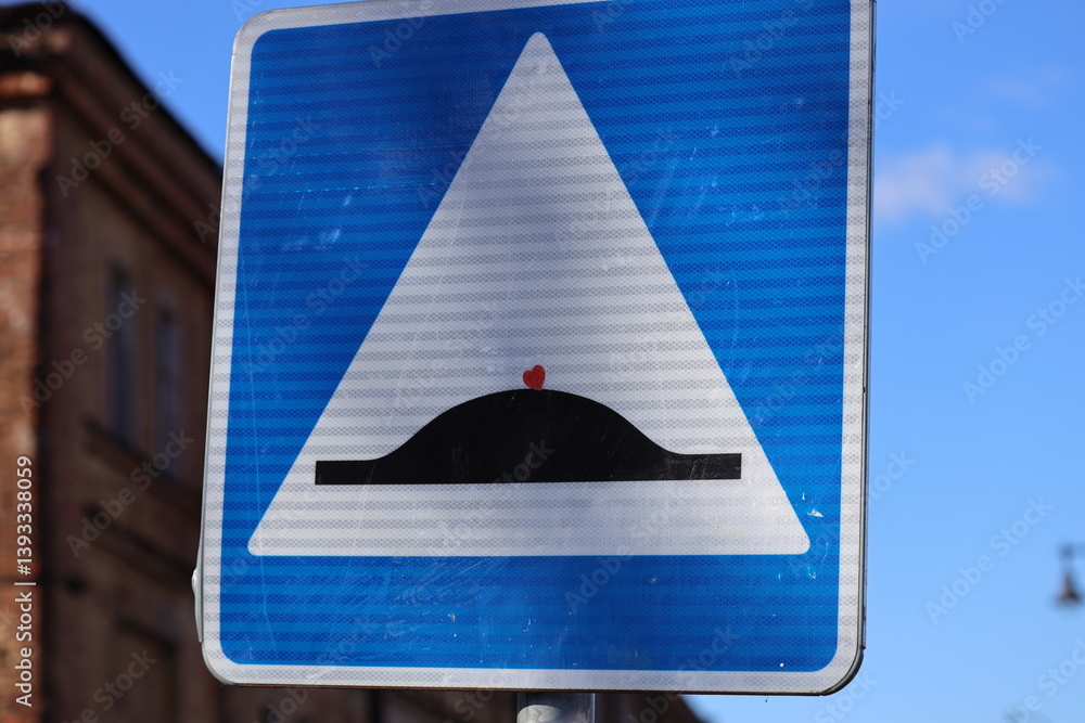 A blue and white street sign with a red dot indicating direction or importance, useful for navigation and wayfinding.