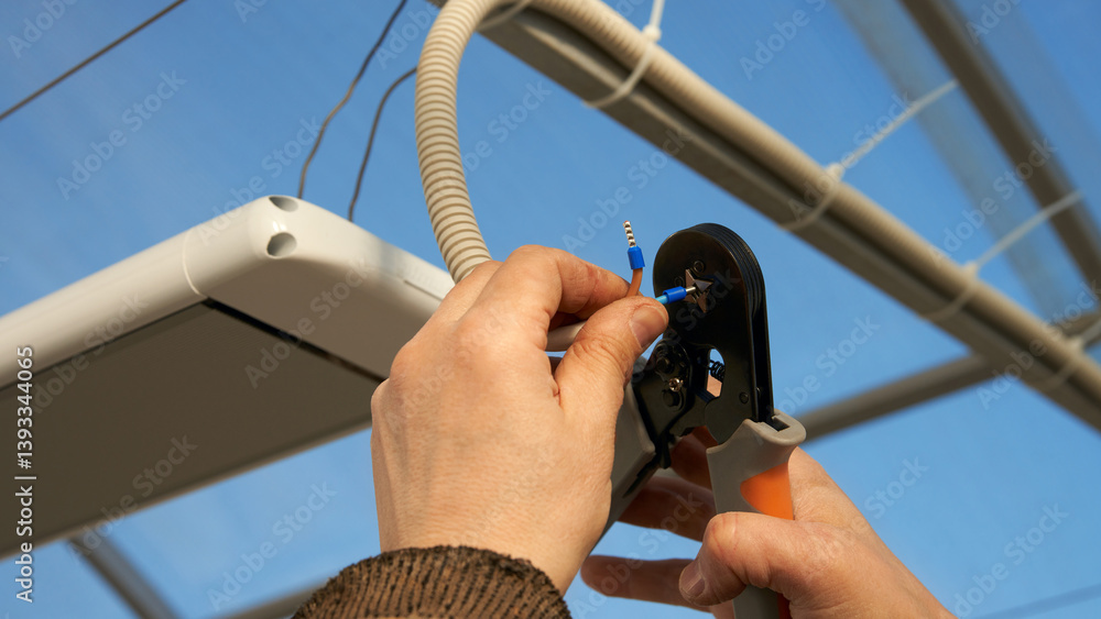 Installation of infrared heater in the greenhouse. Bringing the electrical cable. A man crimps the terminal on the contact of the wire.