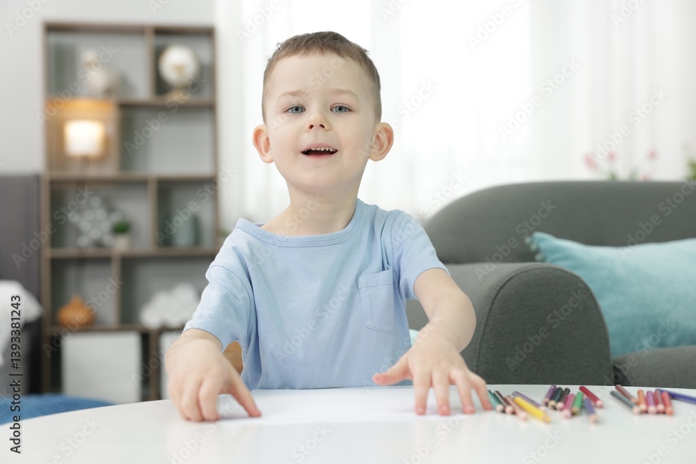 Cute little boy with sheet of paper and colorful pencils at table indoors Cute little boy with sheet of paper and colorful pencils at table indoors