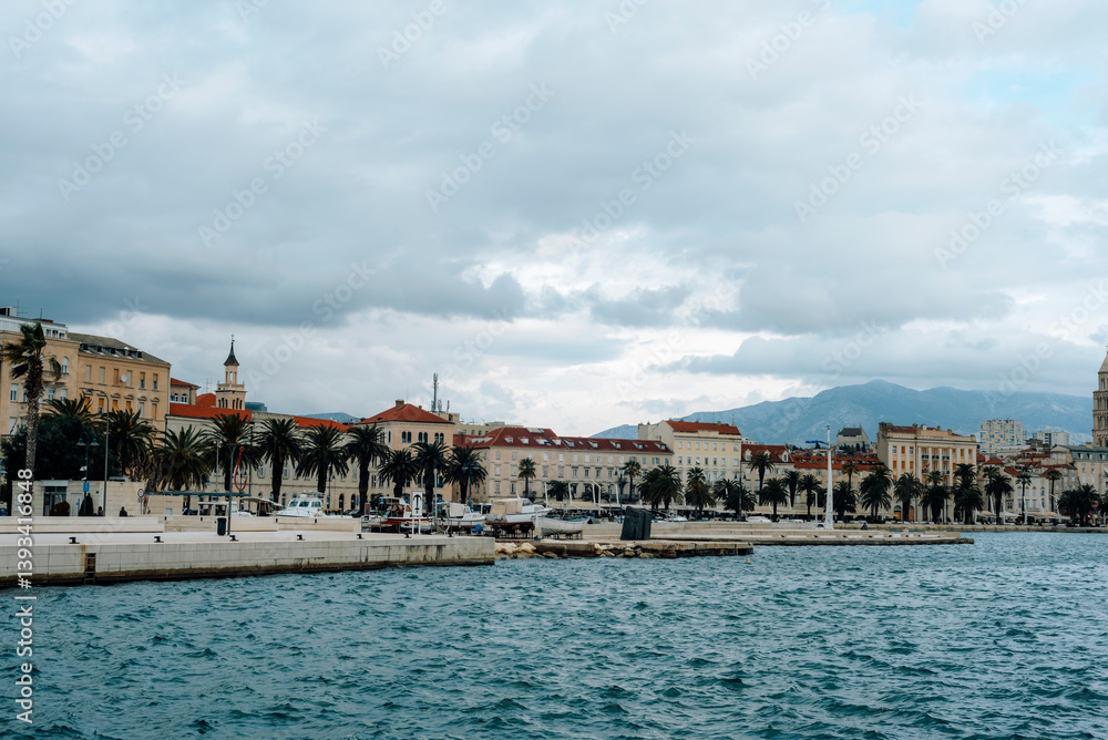 Naklejka premium Seafront promenade with historic buildings and palm trees under cloudy sky. Split, Croatia