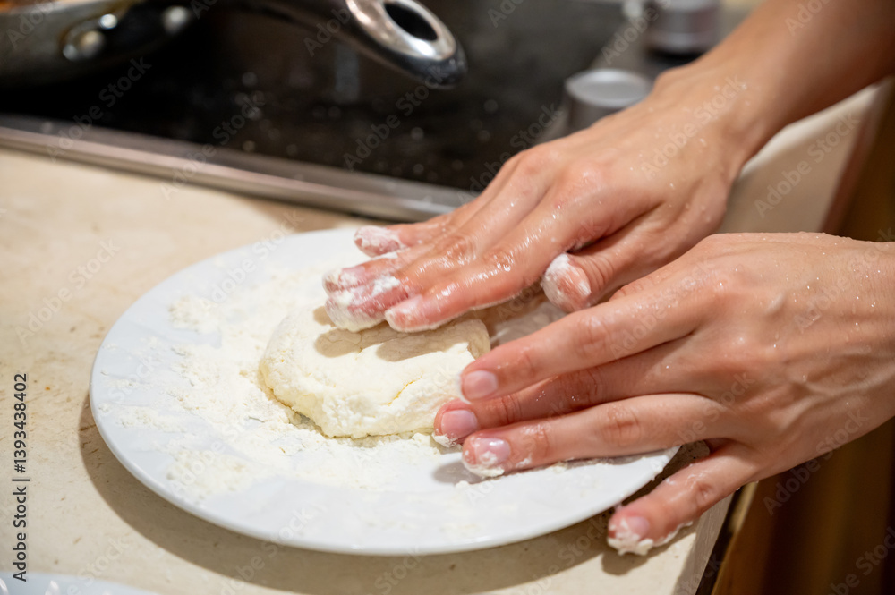 Frying Syrniki – Female Hands Covered in Dough and Flour. Close-up of female hands frying traditional syrniki (cottage cheese pancakes) in a frying pan.