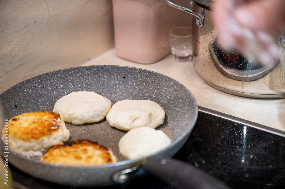 Frying Syrniki – Female Hands Covered in Dough and Flour. Close-up of female hands frying traditional syrniki (cottage cheese pancakes) in a frying pan.