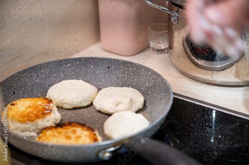 Obraz na płótnie Frying Syrniki – Female Hands Covered in Dough and Flour. Close-up of female hands frying traditional syrniki (cottage cheese pancakes) in a frying pan. w salonie
