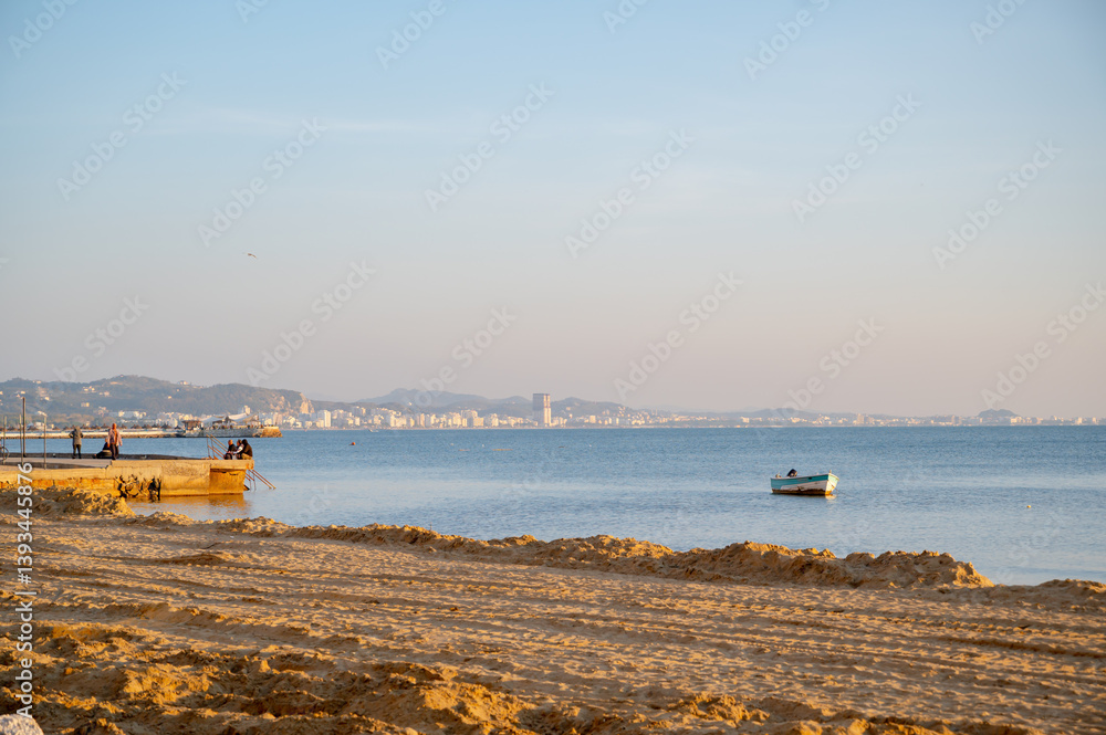 The seashore is under reconstruction and the Adriatic shore in Durres. A fisherman catches fish from a pier.