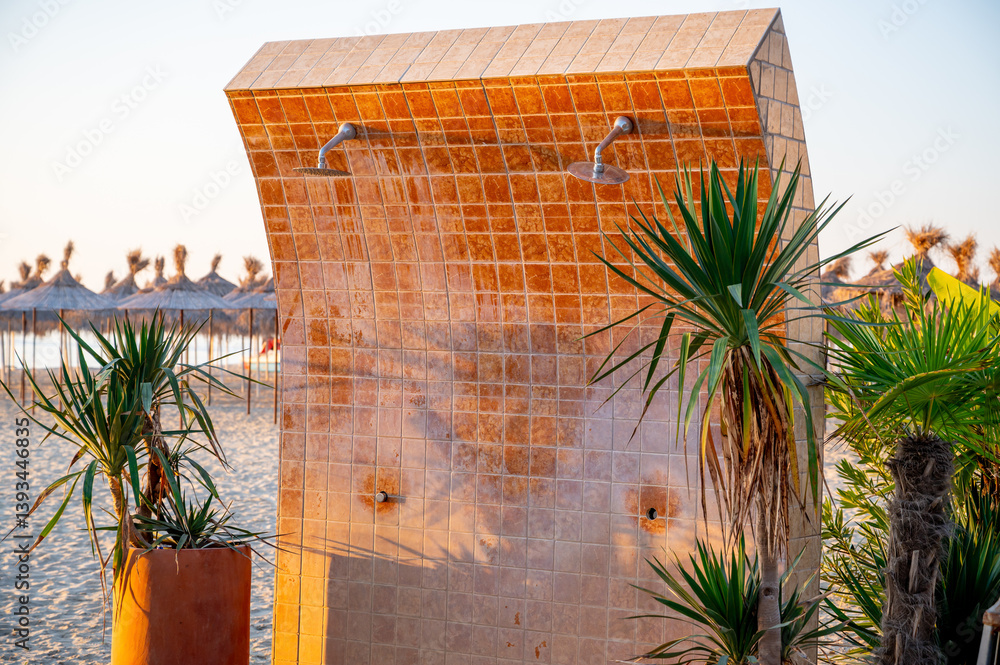 Outdoor shower on a beach, fully tiled with ceramic tiles. Modern and functional seaside utility, designed for public use at a coastal resort or beachfront area.