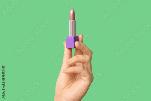 Hand holding lipstick on green background