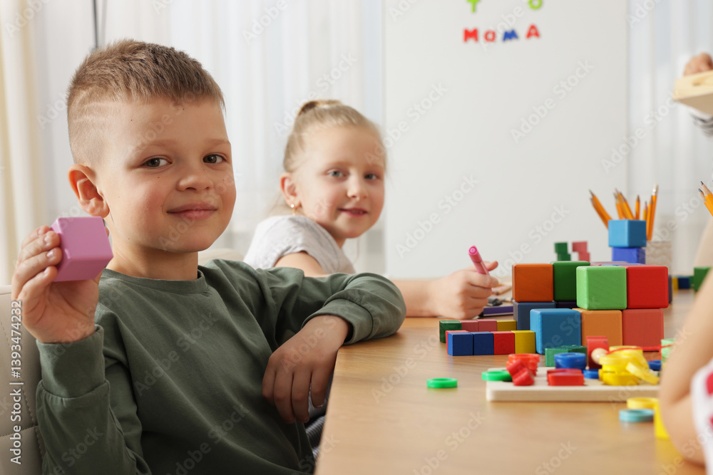 Fototapeta premium Cute boy with cube at desk during lesson in school