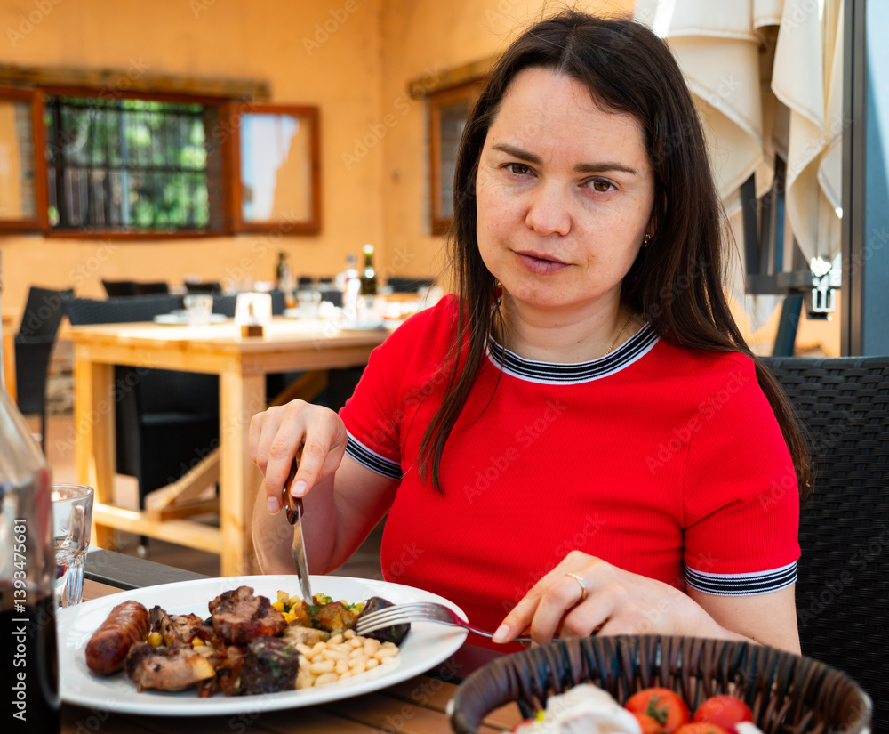 Portrait of woman spending time on open terrace of catalan restaurant and eating traditional parillada de carne Portrait of woman spending time on open terrace of catalan restaurant and eating traditional parillada de carne