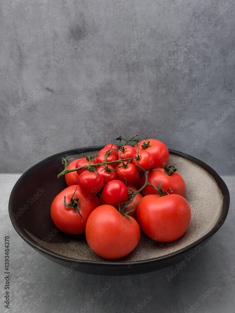 Ripe red tomatoes clustered on vine, nestled in black ceramic bowl, showcasing garden fresh produce against minimalist background wallpaper copy space