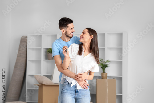Happy young couple with keys from new flat hugging in room on moving day