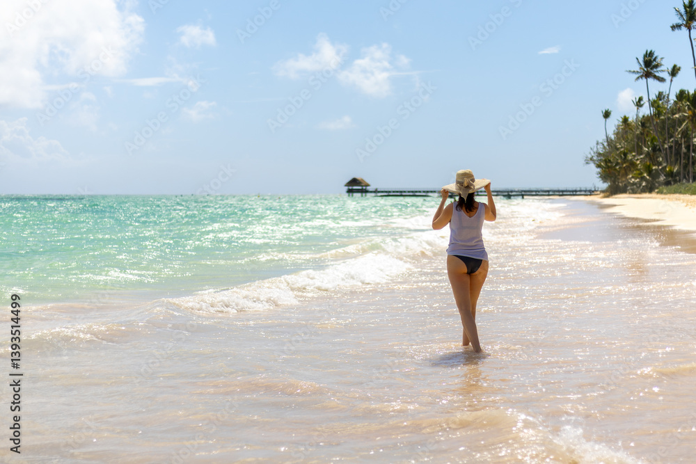 Woman walking along a tranquil beach enjoying warm weather and gentle waves in a tropical paradise Woman walking along a tranquil beach enjoying warm weather and gentle waves in a tropical paradise