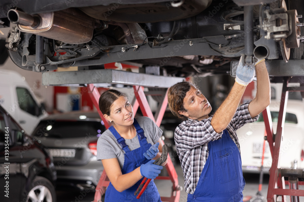 Experienced auto mechanic tells a novice auto mechanic how to properly repair a car at a car service center.