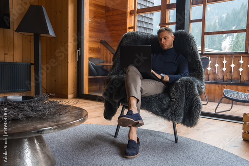 Foto A man sits in a fur covered chair in a wooden hotel room with glass doors, overlooking snow dusted trees and alpine scenery