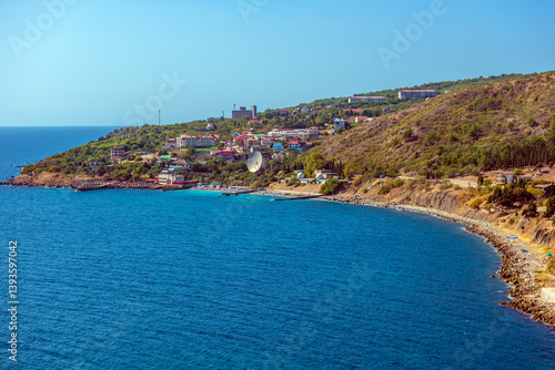 Obraz na płótnie a picturesque seascape of the southern coast of Crimea. The frame captures part of the coast with a bright blue sea, a curved coastline with pebbles and buildings, as well as green hillsides dotted w salonie