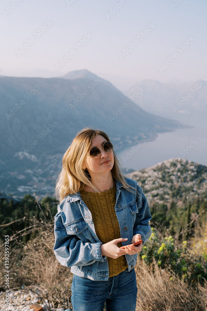 Naklejka premium Woman in sunglasses stands on a mountain above the Bay of Kotor. Montenegro. Top view