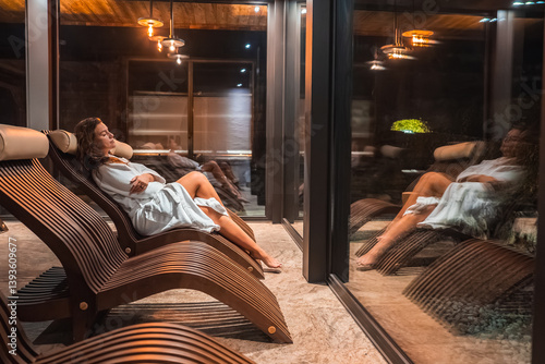 Bilde på lerret A woman in a white robe reclines on a curved wooden lounge chair near a glass window