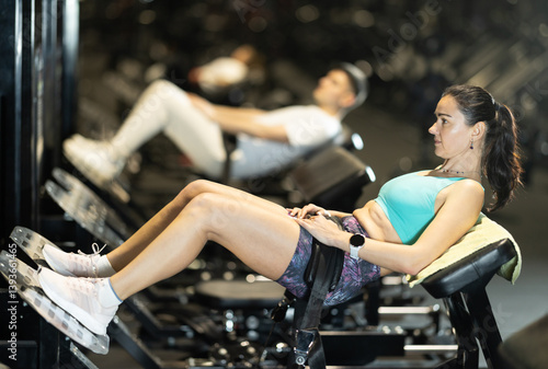 Schilderij op canvas Positive motivated woman performing hip thrusts on glute bridge machine to target glutes and hamstrings during lower body workout at gym