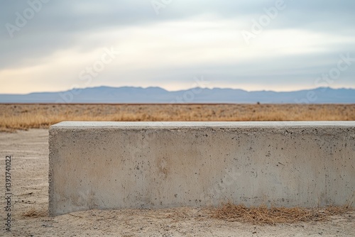 A concrete barrier stands before mountains and a field