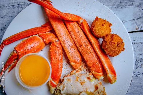 Top view of crab leg with hush puppies and and butter sauce in a white plate.