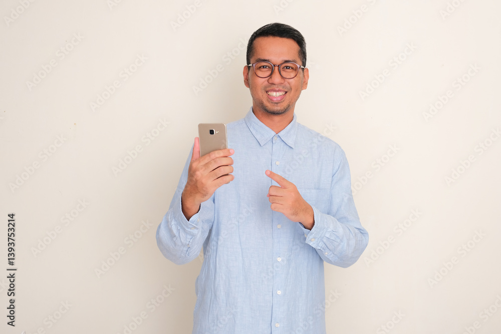 A man smiling and pointing at mobile phone that he hold A man smiling and pointing at mobile phone that he hold