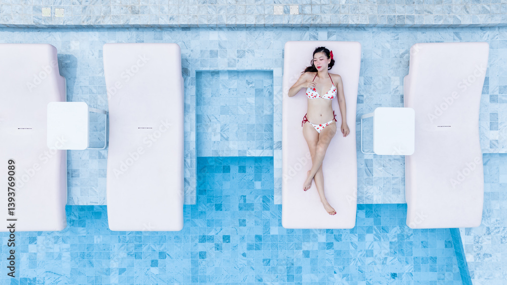 Top view asian woman in bikini lying down on sunbed in swimming pool, Asian woman in bikini relax in swimming pool in hotel resort sunbathing at hotel, Summer and holiday vacation trip.