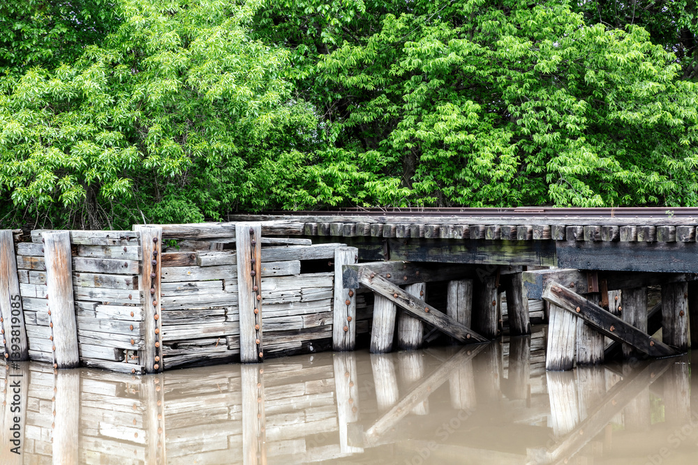 Wooden trestle for railroad tracks, spanning a stream in Cloud County, Kansas, Reflection of structure on the water. Green trees in the background.
Wooden trestle for railroad tracks, spanning a stream in Cloud County, Kansas, Reflection of structure on the water. Green trees in the background.