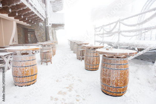 Fotografie Snow-covered winter outdoor dining area with frosted barrels and tables