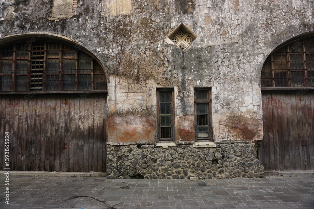 Fototapeta premium Old weathered building facade, wood doors, stone base, urban setting, historical architecture