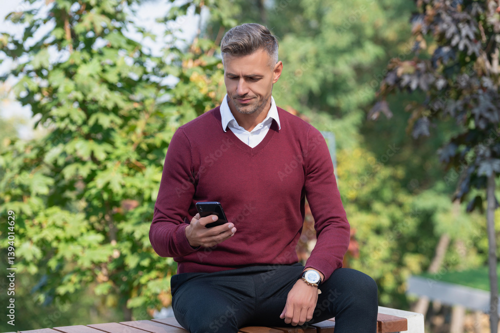 Mature man use mobile phone. Businessman use phone outdoor. Sitting mature business man. Autumn style. Businessman in autumn park. Caucasian man has business casual style. Texting a message Mature man use mobile phone. Businessman use phone outdoor. Sitting mature business man. Autumn style. Businessman in autumn park. Caucasian man has business casual style. Texting a message